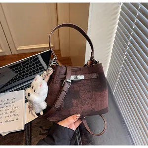 Detailansicht einer braunen Eimertasche mit Textur und einem weißen Plüschhund-Schlüsselanhänger
