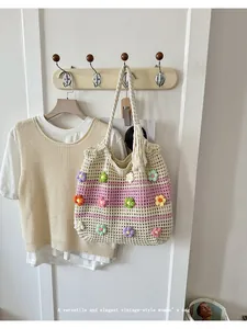 Détail d'un sac cabas crocheté main avec appliqués de fleurs colorées suspendu au mur.