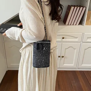 Elegant tweed crossbody phone bag with chain strap worn by a woman in a stylish home setting
