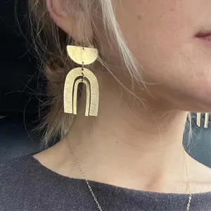 Gros plan de boucles d'oreilles bohèmes en arc doré avec une finition en métal brossé.