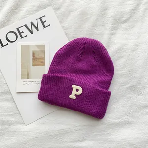 Close-up of a purple knitted beanie with a white embroidered letter P on the cuff