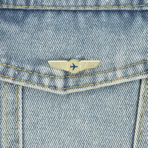 Nahaufnahme eines goldenen Vintage-Ansteckpins mit Pilotenflügeln auf Denim-Stoff