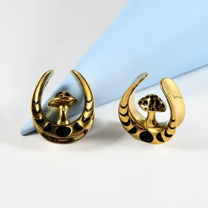 Close-up of gold U-shaped ear gauges featuring black mushroom and moon phase design