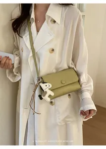 Elegante borsa a tracolla minimalista verde oliva con ciondolo cane su trench bianco