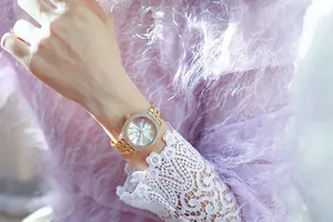 Primer plano de reloj de mujer dorado con bisel de pedrería y manga de encaje lavanda.
