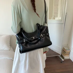 Close-up detail of a large black leather tote bag with buckle strap worn by a model