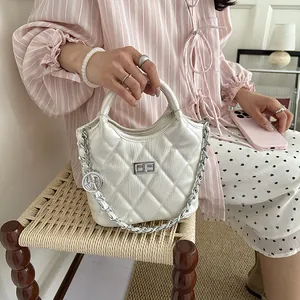 Stylish white quilted bucket bag with silver chain strap and turn-lock held by a model.