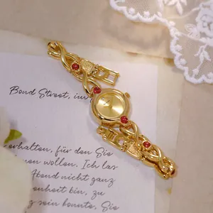 Elegante reloj vintage dorado para mujer con gemas rojas sobre un fondo de encaje delicado