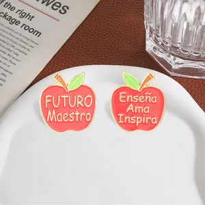 Close-up of red apple enamel pins with Spanish inspirational text for teachers