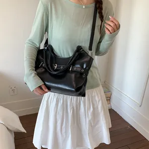Stylish black faux leather tote bag with buckle detail carried by a model in casual outfit.