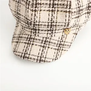 Close-up detail of plaid newsboy cap featuring a gold heart-shaped button accent.