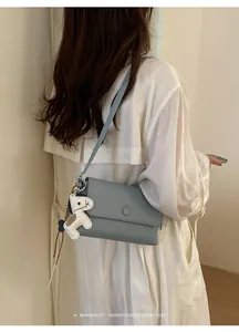 Modella elegante che indossa una borsa a tracolla minimalista azzurra con ciondolo a cane