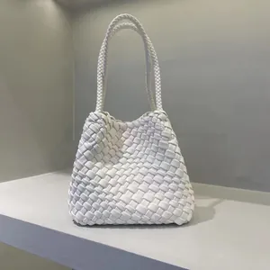 Elegant white woven bucket bag with braided straps in a minimalist studio setting