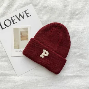 Close-up of a burgundy knit beanie with a white P embroidered patch on a white background.