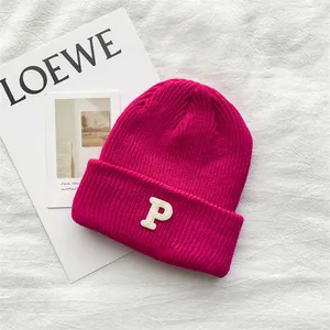 Detailed view of vibrant magenta knitted beanie with white embroidered letter P decoration