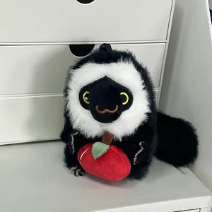 Detalle de un lindo llavero de peluche de mono blanco y negro que sostiene una manzana.