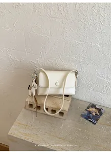 Dettaglio di borsa sottobraccio bianco crema con un simpatico ciondolo a cane.