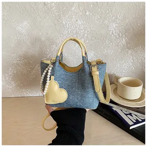 Stylish denim bucket bag with yellow heart charm and pearl strap detail view.