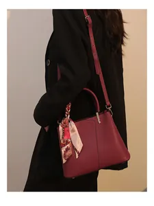 Close-up detail of the elegant red handbag featuring a stylish scarf and sturdy metal hardware.