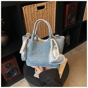 Stylish denim tote bag featuring silver handles and a dainty pearl heart charm.