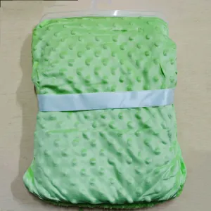 Vue détaillée d'une couverture verte pliée à pois Minky avec ruban blanc et cintre