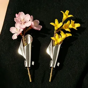 Unique silver cone brooch pins holding fresh pink and yellow flowers on black fabric.