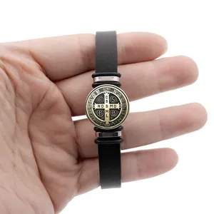 St. Benedict Medal charm on black leather snap bracelet shown being held by hand