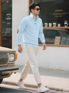 Side view of a man walking in a light blue jacquard knit sweater with elbow patches.