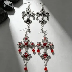 Dettaglio di orecchini a croce gotica con cristalli rossi e neri in finitura argento antico.