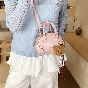 Close-up detail of stylish pink bowling bag with teddy bear charm worn as crossbody.