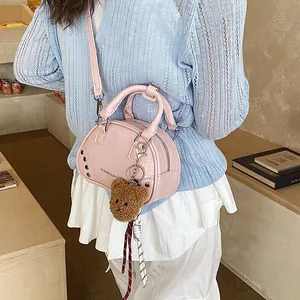 Close-up detail of a stylish pink bowling handbag with silver rivets and bear charm.