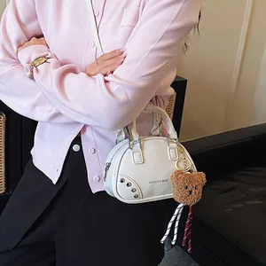 Stylish white mini bowling bag with a cute bear charm shown on a model in a pink cardigan.