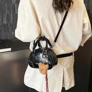 Stylish black glossy bowling bag with a cute teddy bear charm, shown worn by a model.