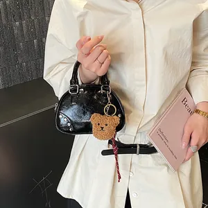 Black patent leather bowling handbag with silver studs and a brown teddy bear keychain charm