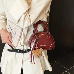 Detail view of a stylish burgundy bowling handbag featuring a cute plush bear keychain.