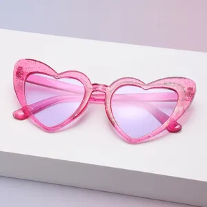 Detailansicht einer herzförmigen rosa Glitzer-Sonnenbrille mit lila Gläsern auf weißem Block
