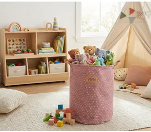 Pink polka dot cotton linen laundry hamper used as a plush toy storage bin in a nursery.