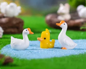 Close-up of miniature resin white goose and yellow duckling figurines on blue sand.