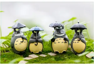 Detailansicht von vier Totoro-Figuren mit Regenschirmen in einer Mooslandschaft