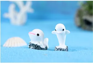Detailweergave van twee mini witte dolfijnbeeldjes van hars op zacht blauw zand