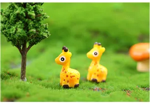 Close-up of two miniature resin giraffe figurines in a green moss micro-landscape.