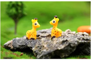 Close-up of two miniature resin giraffe figurines in a green moss micro landscape