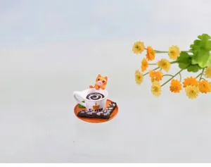 Detail van miniatuur kattenbeeldje met koffiekopje en koekje op een oranje bordje