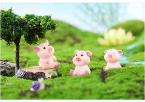 Close-up view of three cute pink resin pig figurines sitting on miniature mossy grass