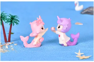 Detail of cute mermaid couple figurines in a blue sandy micro-landscape scene.