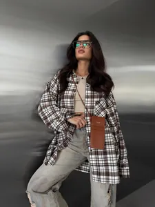 Detailopname van een vrouw in een bruin geruit oversized casual shirt met mouwen.