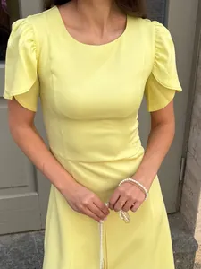 Detail view of pale yellow dress featuring elegant petal sleeves and fitted waist design.