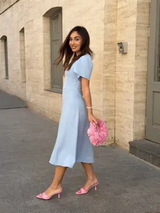 Elegant light blue midi dress with waist-cinching design featuring pink accessories in outdoor setting