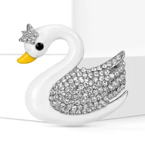 Dettaglio di un'elegante spilla a cigno bianco con ali di strass e una corona d'oro.