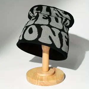 Schwarze Strickmütze mit grauen Buchstabenmustern auf einem Holzständer für den Winter.